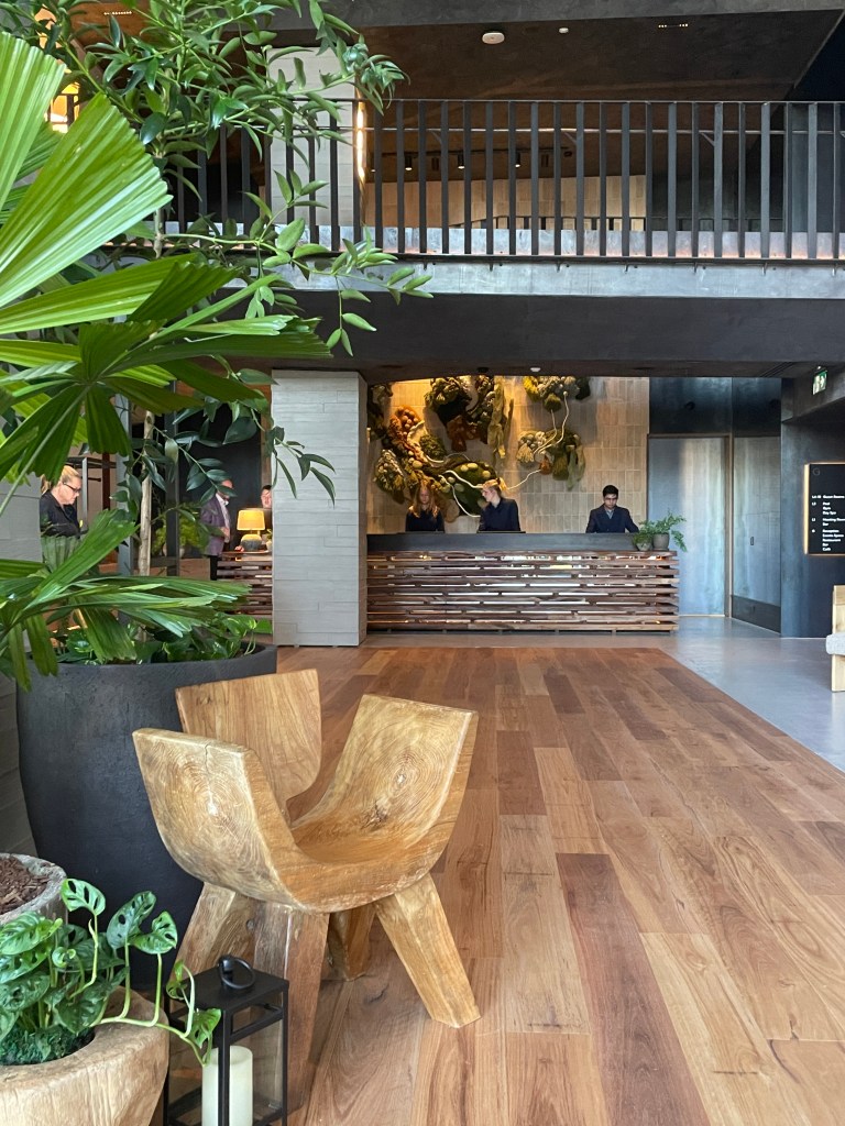 Interior view of the 1 Hotel Melbourne lobby featuring wooden floors, stylish wooden furnishings, and lush greenery.