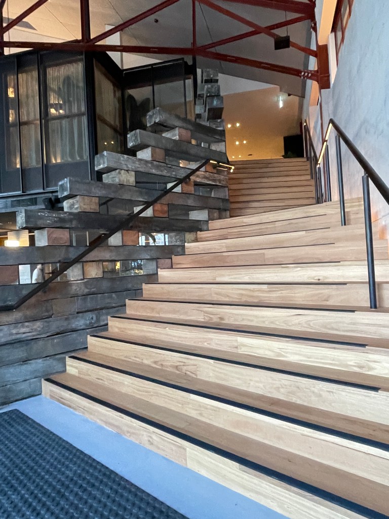 Interior view of a staircase with reclaimed wooden steps and metal railing, featuring a mix of rustic and modern design elements.
